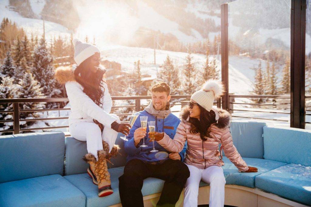 Dreiköpfige Gruppe, die Champagner in Winterkleidung auf der Dachterrasse des W Aspen in Colorado trinkt