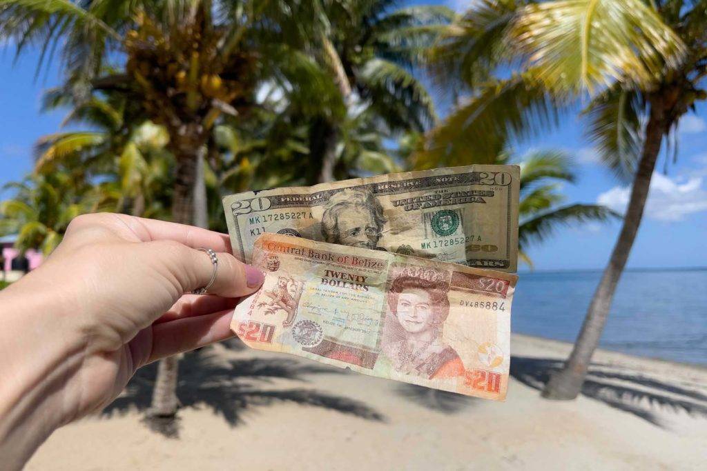 Mujer sosteniendo dos billetes de papel moneda. Un dólar estadounidense de $20 (USD) y un dólar beliceño de $20 (BZD)