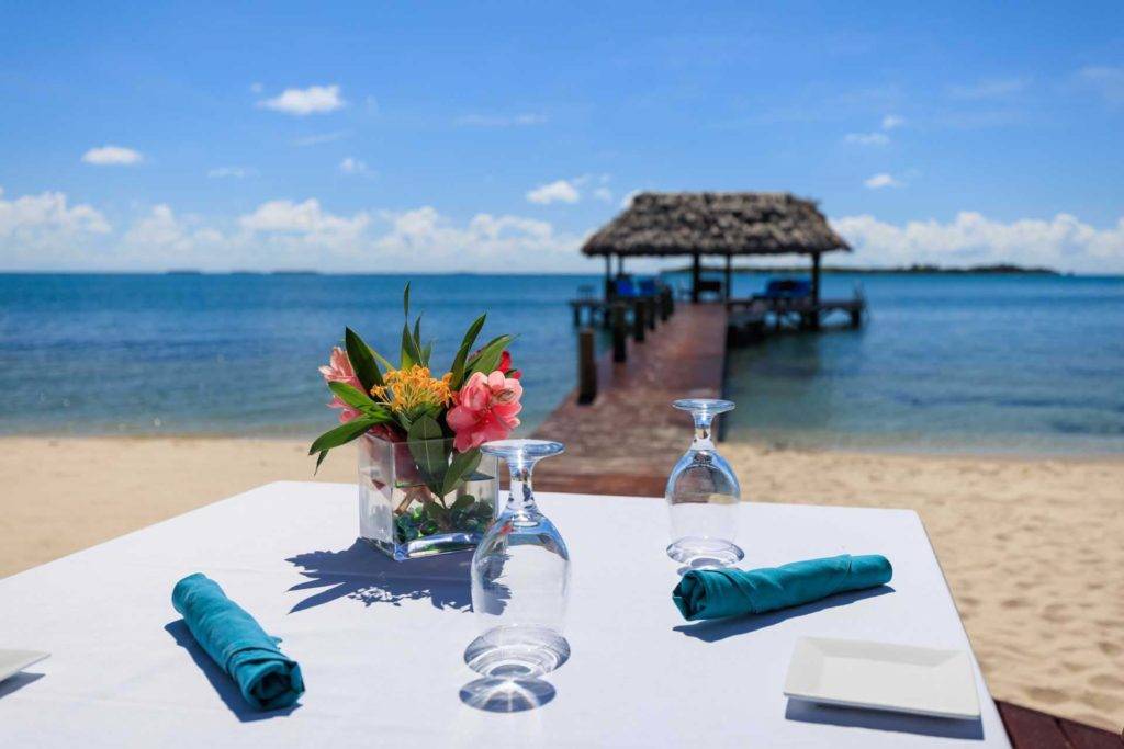 Ponga una mesa de comedor en la playa con vista al muelle cubierto y al océano en Chabil Mar Villas