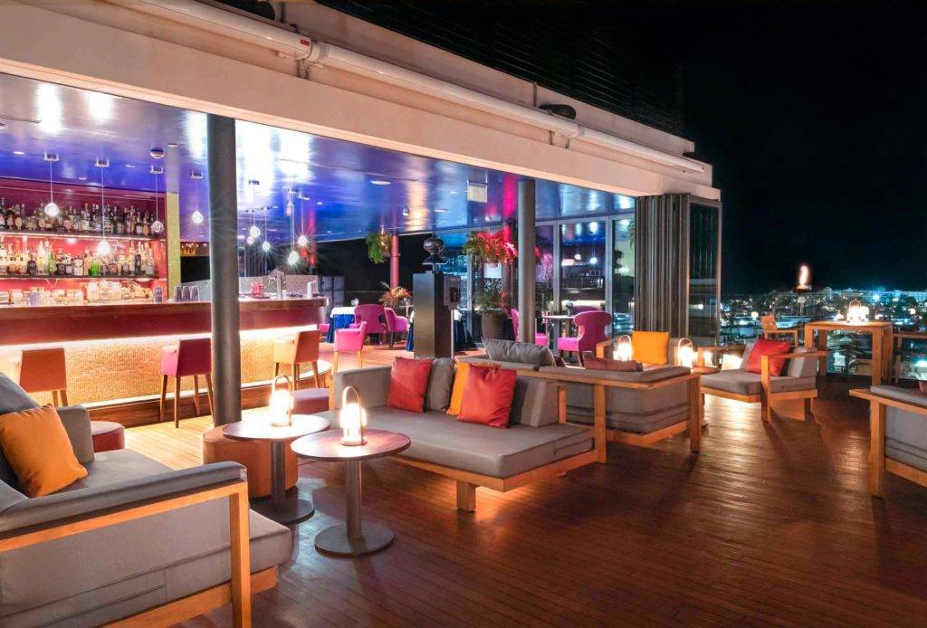 Terraza al aire libre del bar de cócteles Atelier con cómodos sillones iluminados por la noche