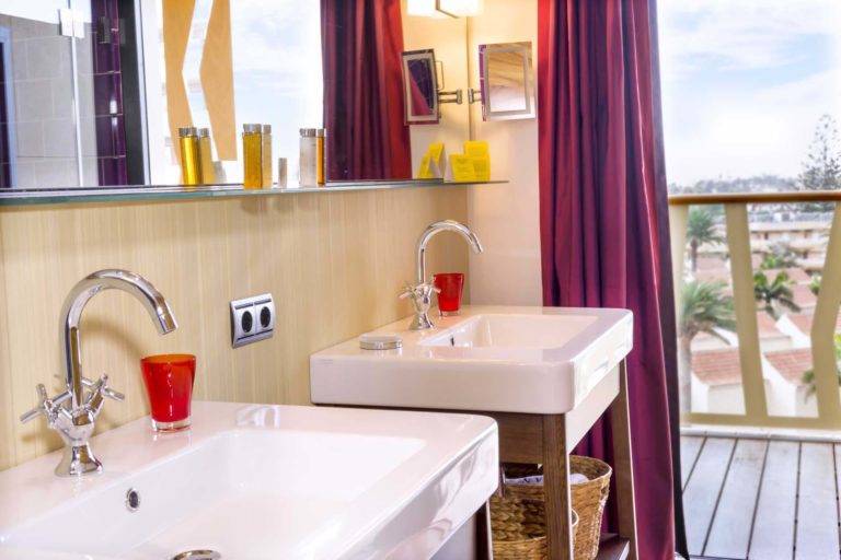 Corner Junior Suite: baño moderno de estilo bohemio con dos lavabos, espejo, artículos de tocador y acceso al balcón | Bohemia Suites & Spa