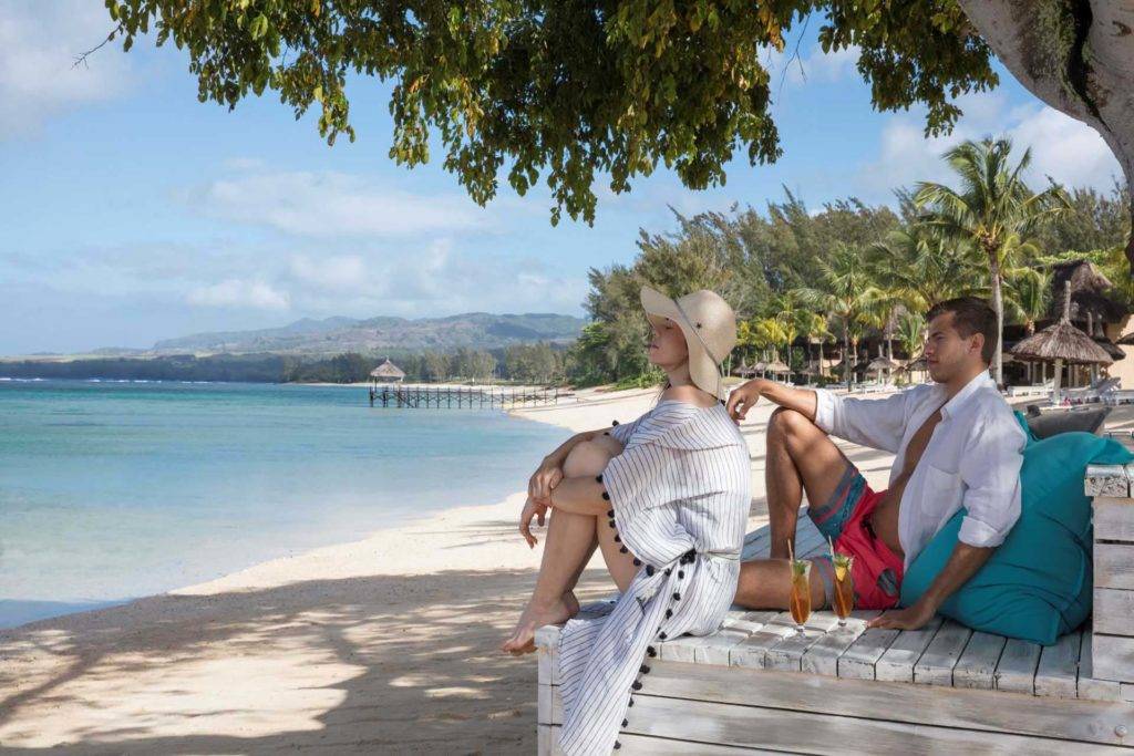 Couple in beach gear sitting on a wooden lounger enjoying the ocean breeze | Shanti Maurice Resort & Spa