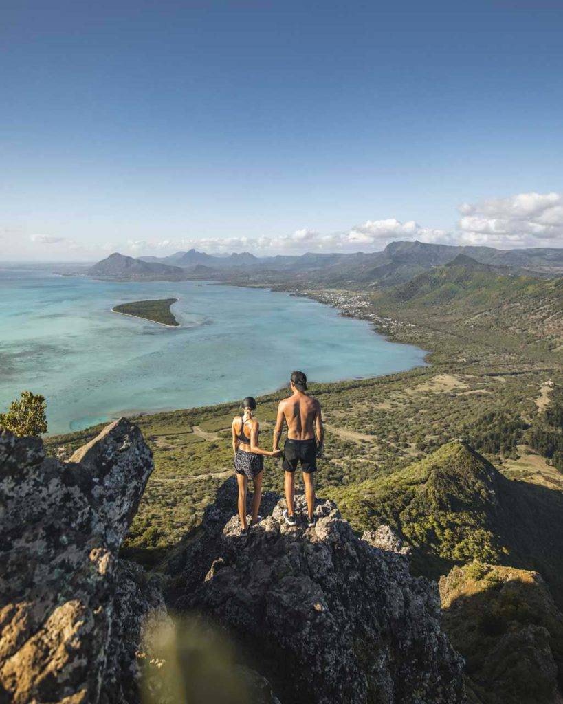 Pareja tomados de la mano en un alto acantilado mientras admira la vista de la isla Mauricio y el océano