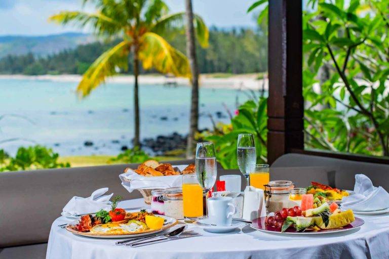 Mesa de comedor cubierta al aire libre con platos de desayuno, fruta, café y jugo | Comidas en la habitación y en la villa en Shanti Maurice Resort & Spa