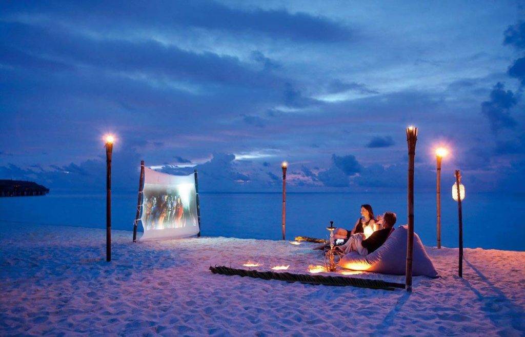 Pareja disfrutando de un cine privado al aire libre en la playa de Shanti Maurice Resort & Spa