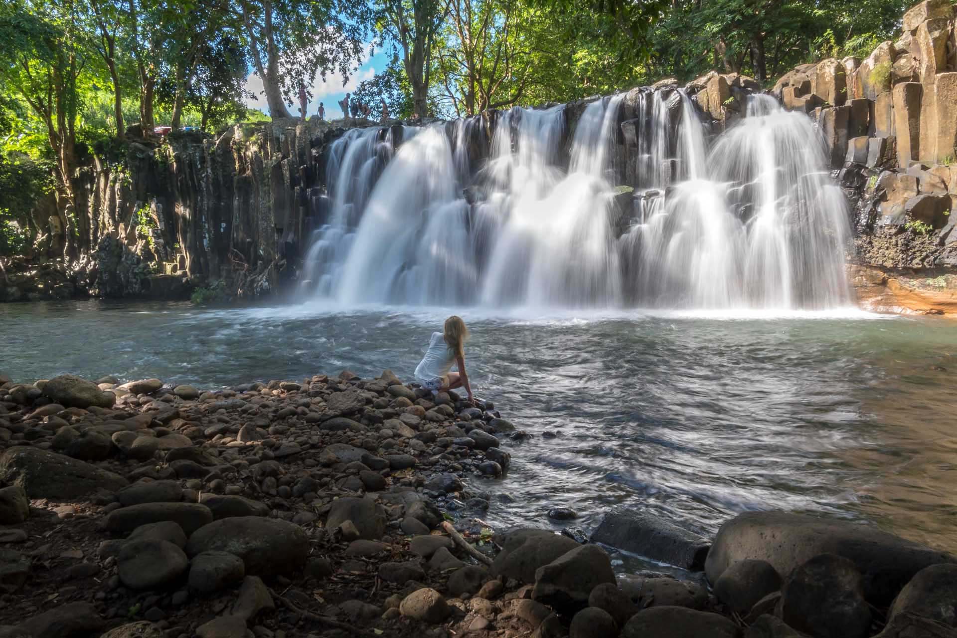 Mujer admirando una cascada natural desde la piscina inferior en Mauricio