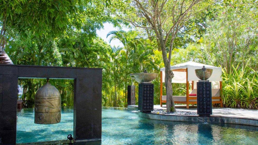 Serena piscina al aire libre rodeada de fuentes, tumbonas y exuberante vegetación | Shanti Maurice Resort & Spa