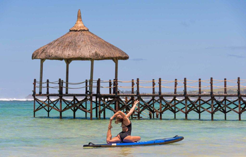 Mujer haciendo yoga en un paddleboard frente al muelle del océano en el Shanti Maurice Resort & Spa