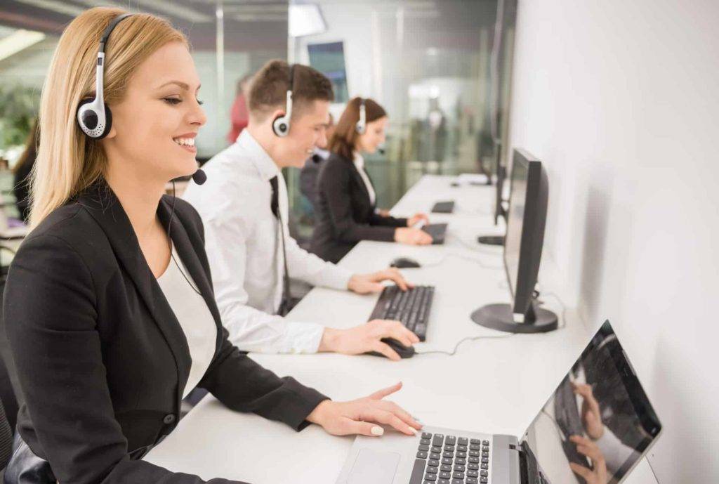 Smiling call center operators in headphones working on laptops