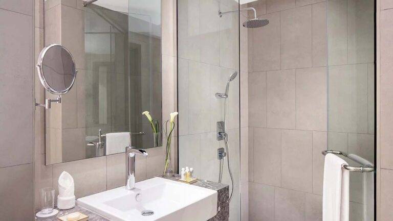 Classic Doppelzimmer – modernes Badezimmer mit Waschtisch, Spiegeln und Regendusche | Erstes Collection Hotel bei JVC