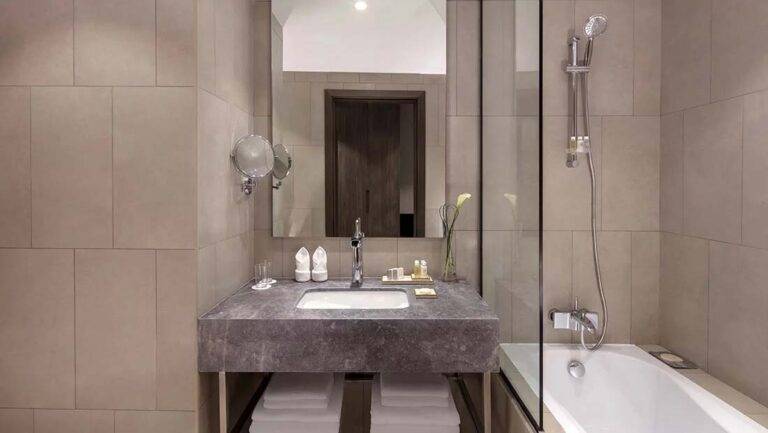 Classic Doppelzimmer – modernes Badezimmer mit Waschtisch, Spiegeln und Badewannen-/Duschkombination | Erstes Collection Hotel bei JVC