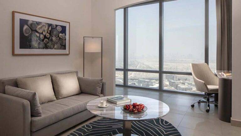 JVC Horizon Suite: sala de estar contemporánea con sofá, estación de trabajo y ventanas grandes | Primer hotel de colección en JVC