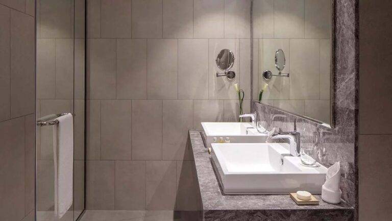 JVC Horizon Suite - contemporary bathroom with double vanity, mirrors, and walk-in shower | First Collection Hotel at JVC