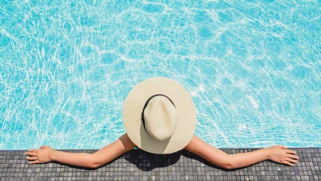 Frau mit Sonnenhut entspannt sich am Rand des Pools im First Collection JVC Hotel