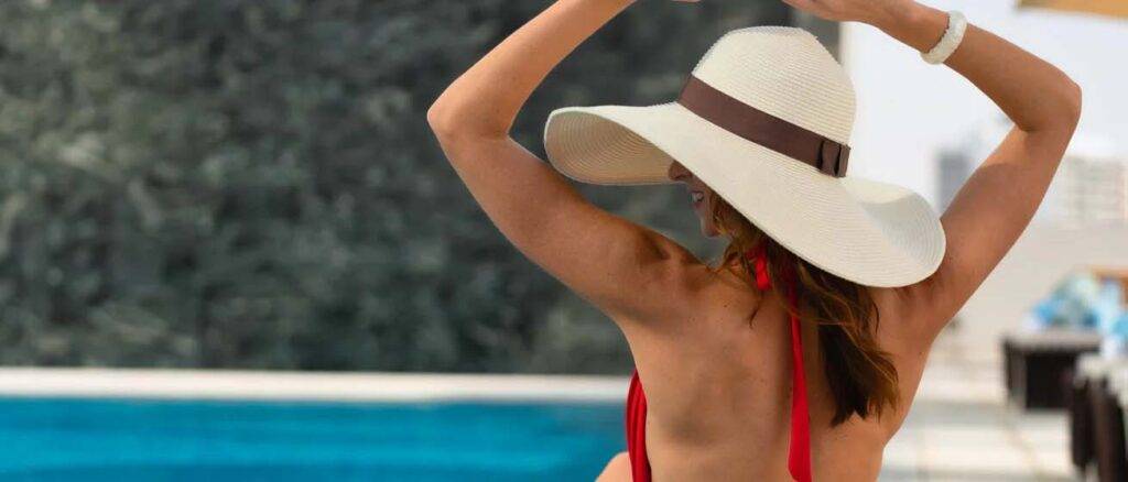 Mujer con sombrero para el sol relajándose al borde de la piscina en el First Collection JVC Hotel