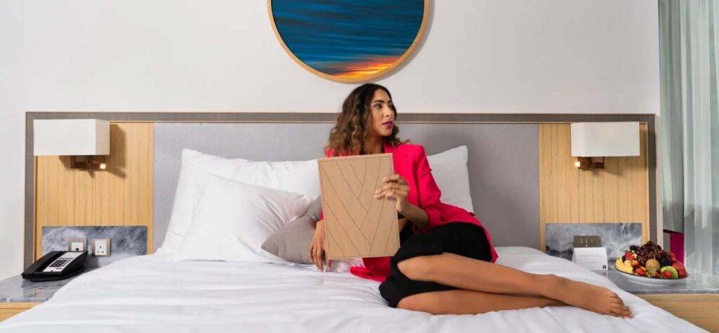 Frau, die sich auf ihrem Hotelbett entspannt und das Zimmerservice-Menü betrachtet | Erste Kollektion JVC Hotel