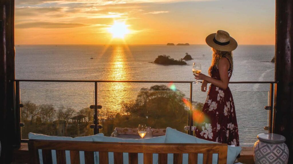 Mujer viendo la puesta de sol en el balcón de su villa privada con una copa de vino | Casa Camaleón en Las Catalinas