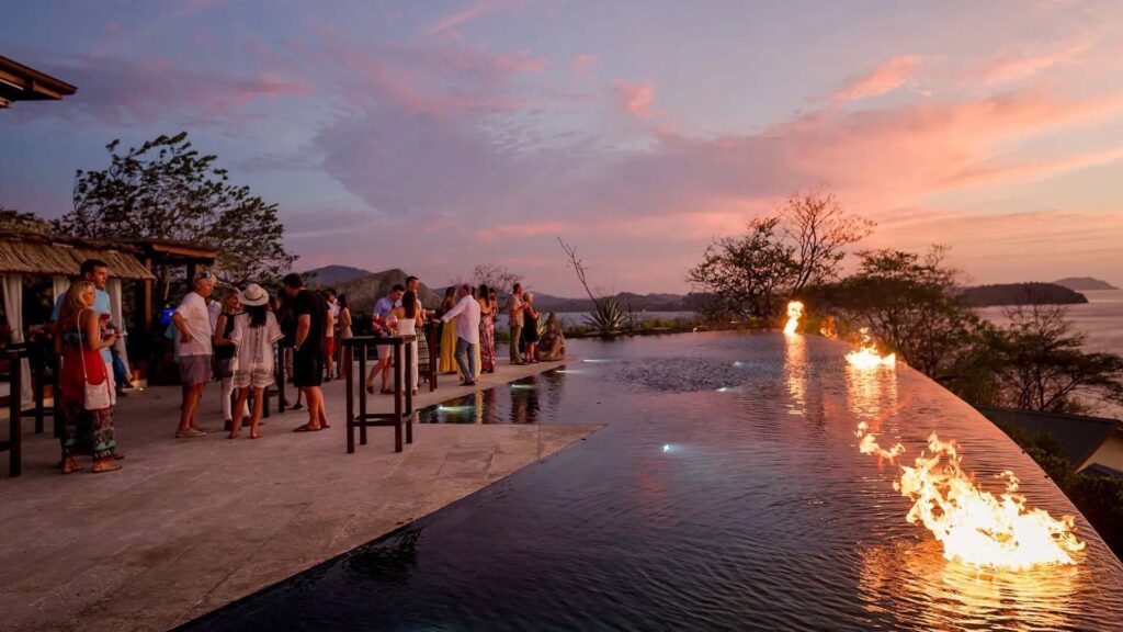 Grupo de personas disfrutando de cócteles en la terraza de la piscina infinita al atardecer | Casa Camaleón en Las Catalinas