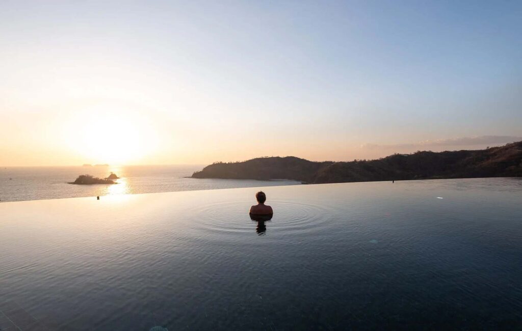 Mujer nadando en la piscina infinita de Casa Chameleon en Las Catalinas admirando la puesta de sol sobre el océano