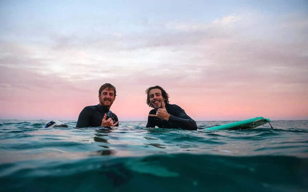 Dos hombres sentados en tablas de surf en el océano al atardecer.