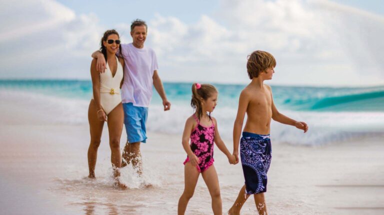 Vierköpfige Familie zu Fuß am Strand entlang im Crane Resort