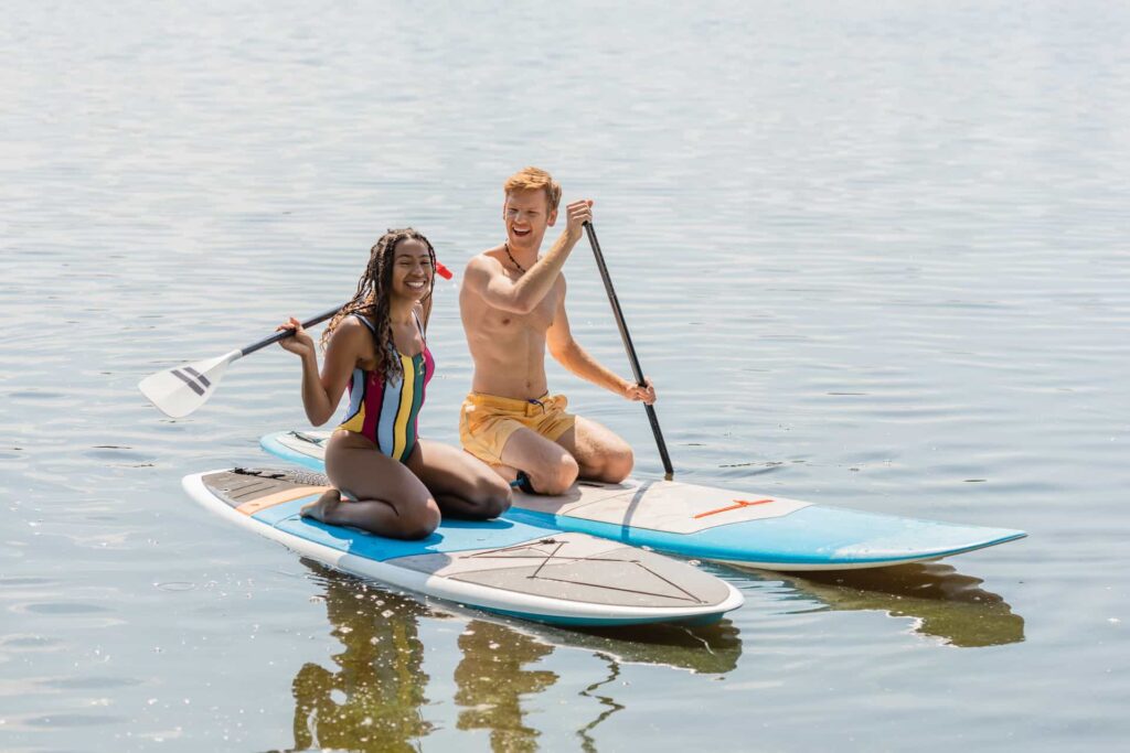 Feliz pareja arrodillada sobre tablas de remo en un lago