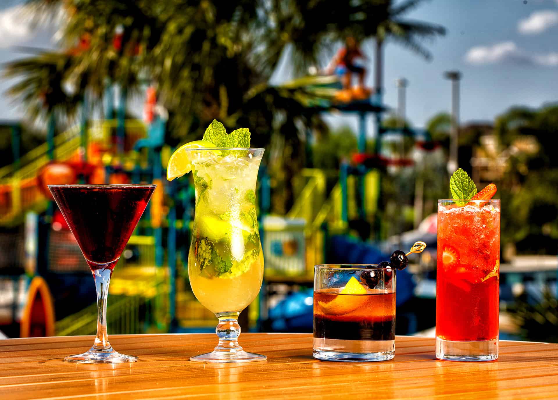 Row of tropical cocktails in varied glasses from Bis Grill at Encore Resort with the colorful water park in the background