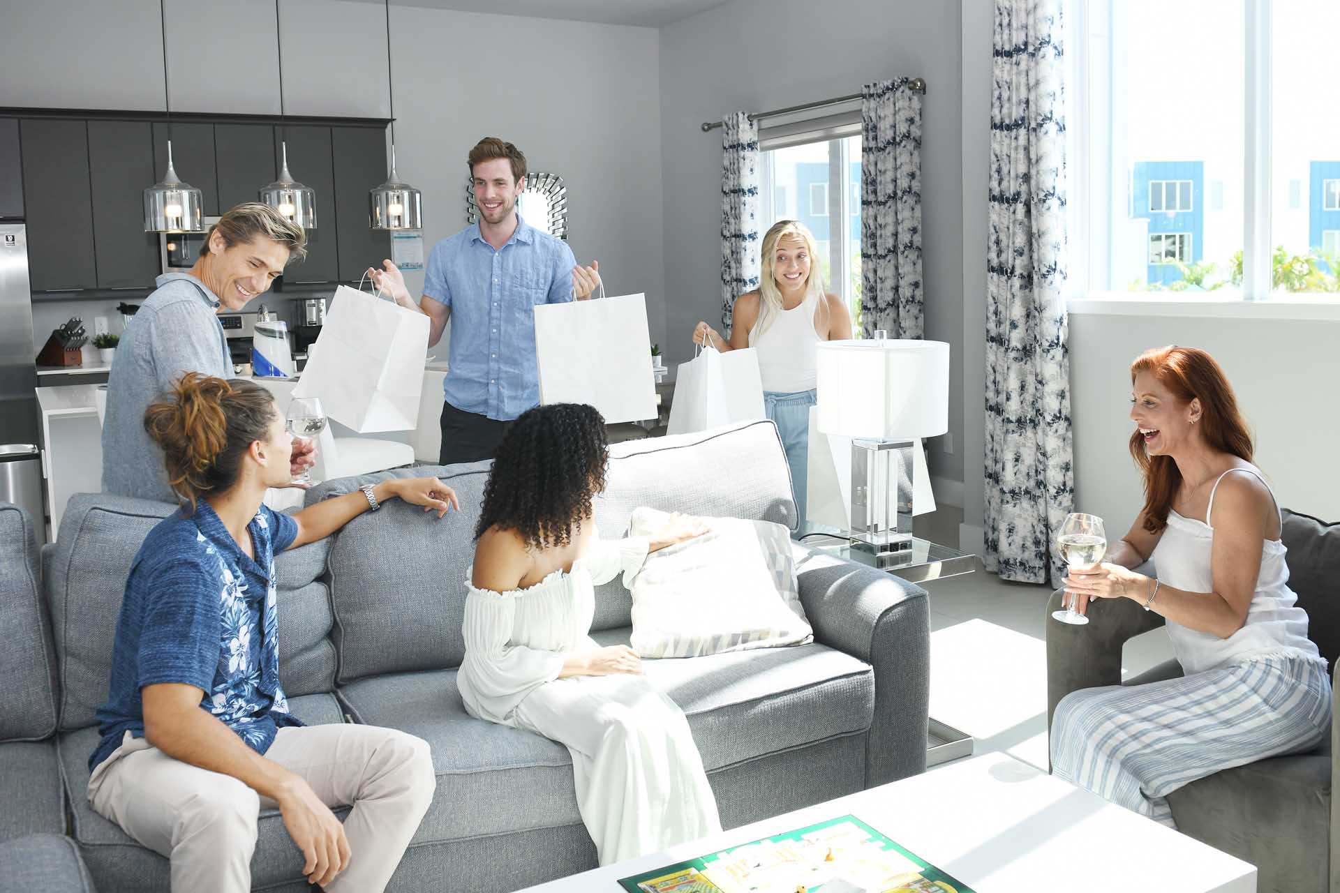 Man and woman bringing in take-out bags to their friends sitting in a living room