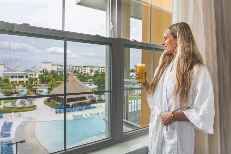 Woman holding a glass of orange juice, admiring the view of the pool from her suite