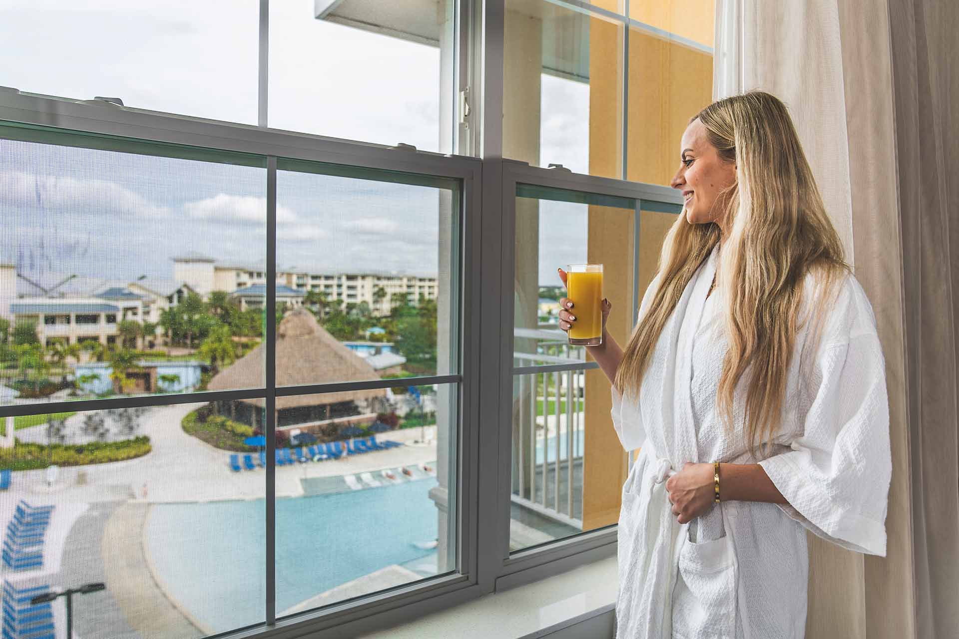 Woman holding a glass of orange juice, admiring the view of the pool from her suite